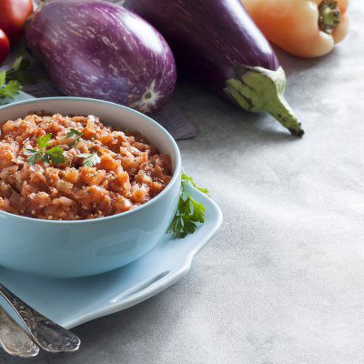 Eggplant caviar in blue bowl and fresh vegetables on background