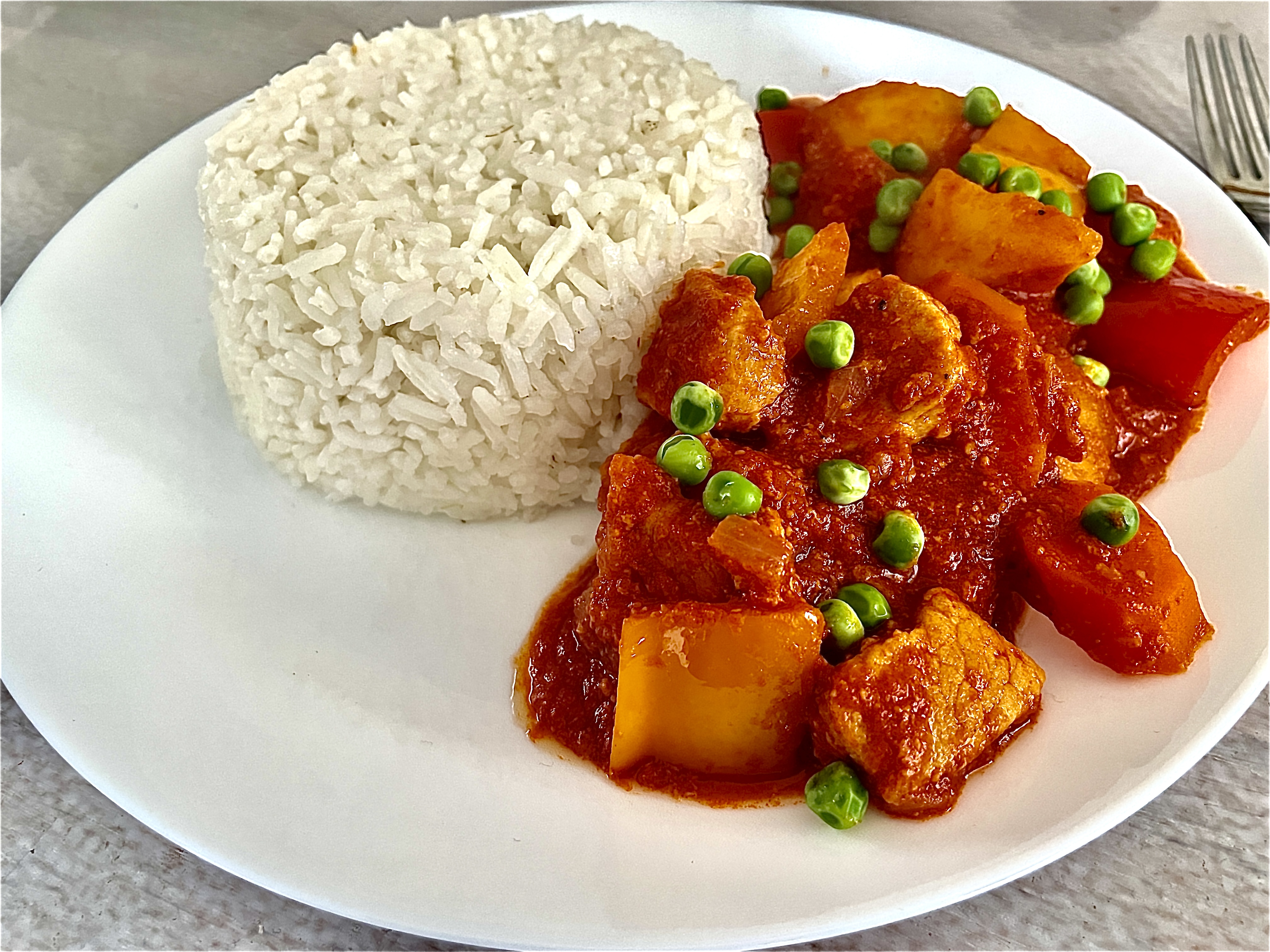 Pork Caldereta with peas and rice served on a white plate